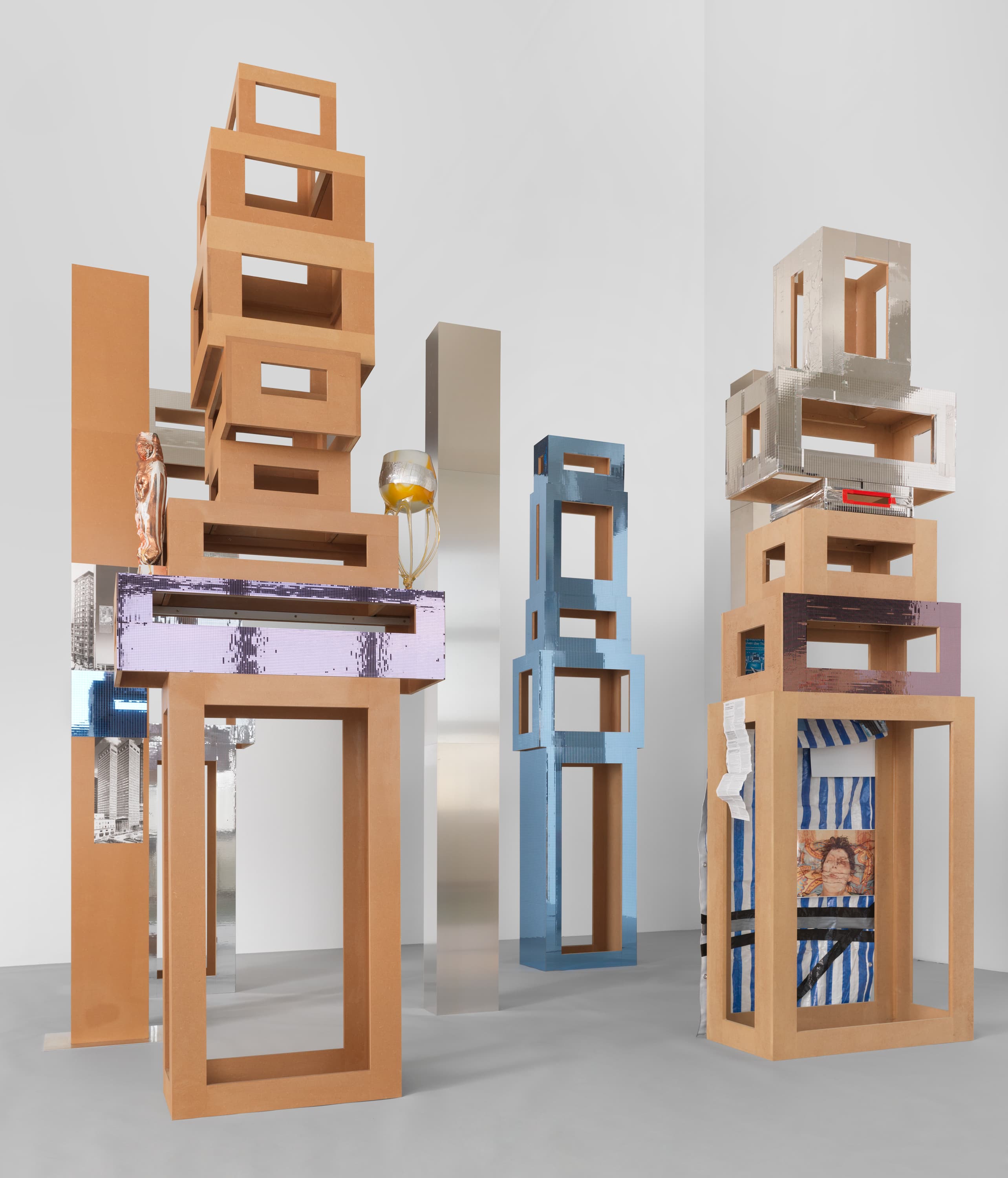 Isa Genzken, Untitled (4 Türme, 3 Stelen), 2015. Installation of 7 parts (4 towers, 3 columns), MDF, plastic, mirror foil, glass, cigarette, tin foil, spray paint, plaster, acrylic, adhesive tape, photographs, metal, aluminium, paper; dimensions variable, approx. 132 ⅘ × 141 ¾ × 118 inches. Courtesy the artist and Galerie Buchholz.